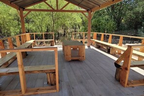 A wooden deck with benches and a table, surrounded by a metal fence and trees. - Vigilante Inn Covered Wagon (Tombstone)