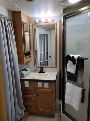 A bathroom with a wooden vanity, a white sink, a mirror, and a glass shower enclosure. - Vigilante Inn Covered Wagon (Tombstone)