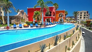 A large, curved swimming pool with blue tiles, surrounded by lounge chairs and palm trees. - Hacienda Encantada by Naya Homes (Cabo San Lucas)