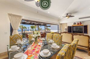 A dining area with a glass table set for six, a sofa with patterned cushions, and a television on the wall. - Hacienda Encantada by Naya Homes (Cabo San Lucas)