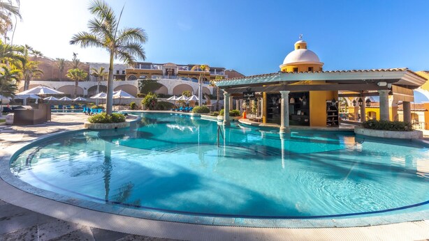Ein Poolbereich eines Resorts mit klarem, blauem Wasser, Palmen und einem Pavillon.