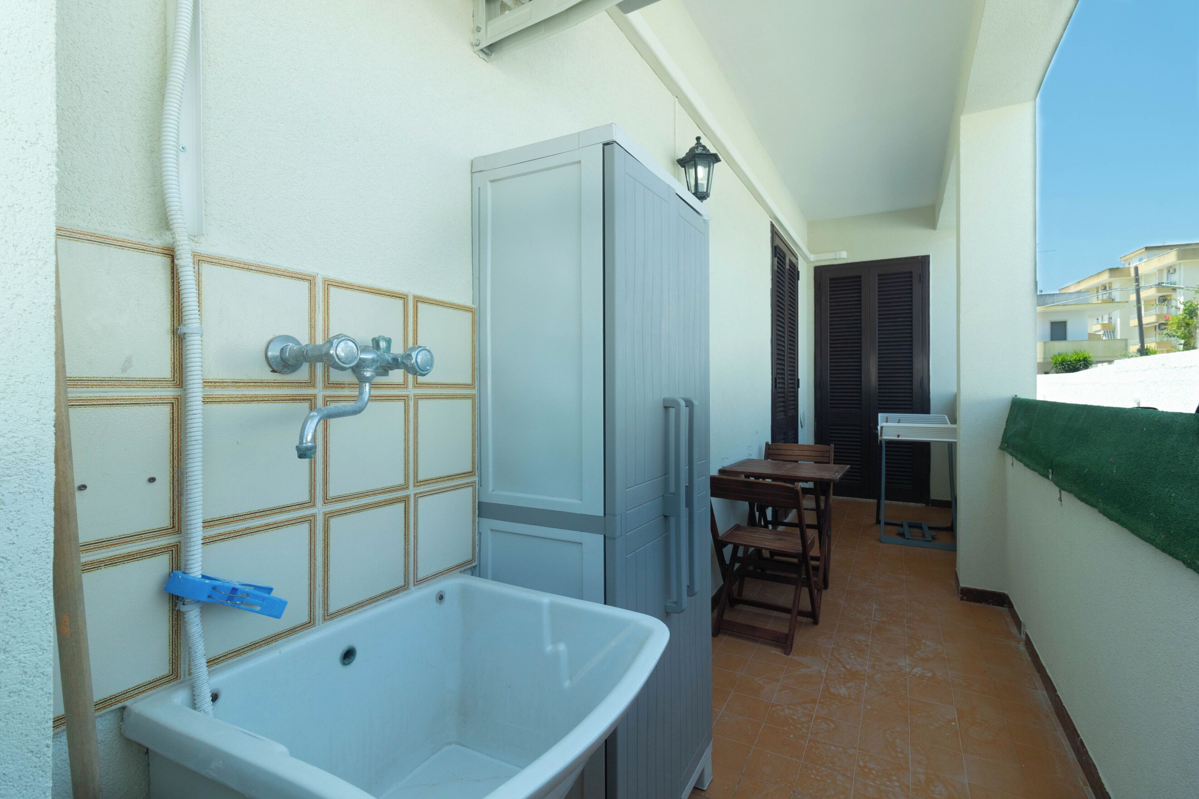 Un baño pequeño con un lavamanos blanco, un armario y una ducha. Fuera del baño hay una mesa y sillas.
