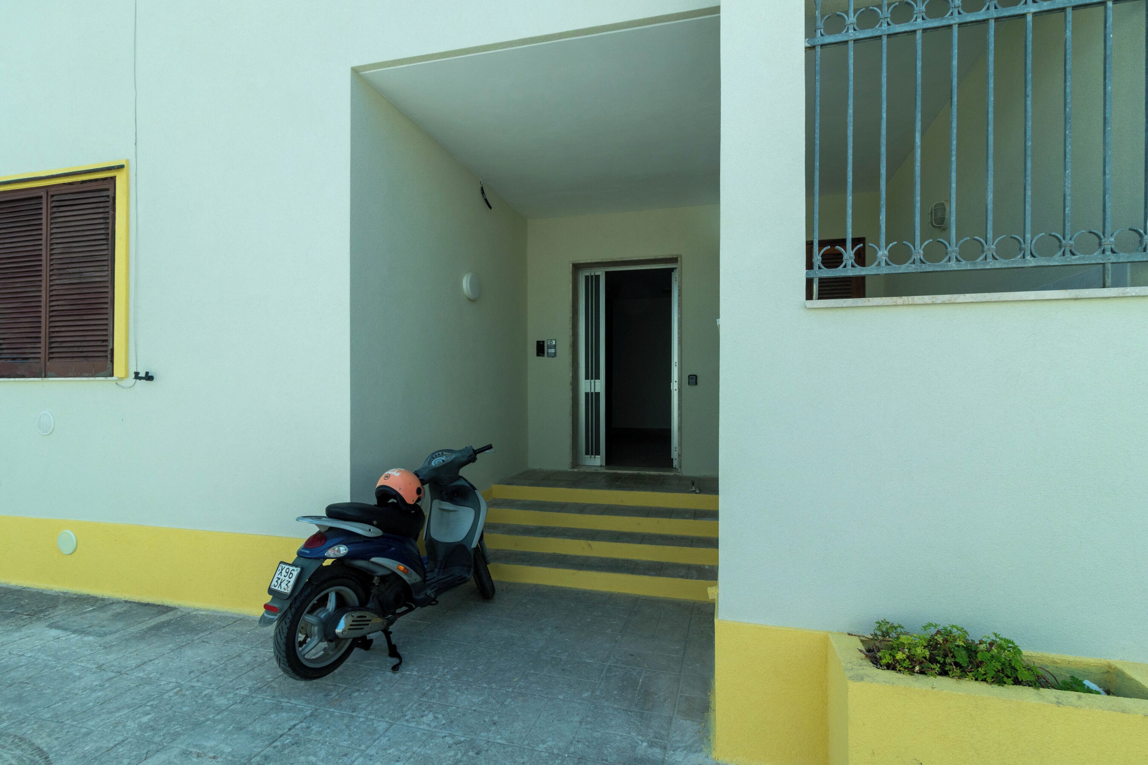 A scooter parked outside a building with a yellow and white facade, a door leading to an interior, and a window with metal bars.