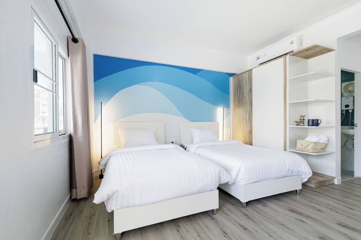 Een hotelkamer met twee bedden, een groot raam, een muurschildering en een kledingkast.