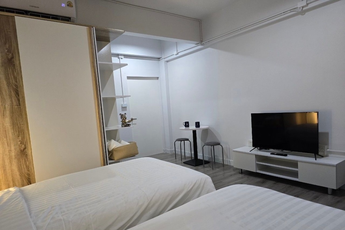 A hotel room with two beds, a TV, a small table with two chairs, and a wardrobe.