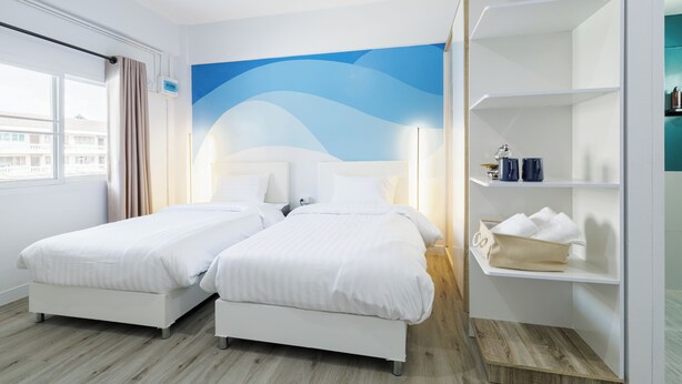Une chambre d’hôtel avec deux lits, une grande fenêtre, une fresque murale et une étagère intégrée où sont rangés les articles de toilette.