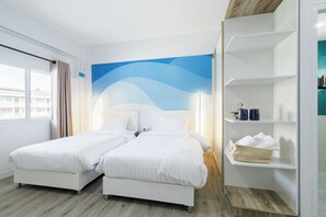 Een hotelkamer met twee bedden, een groot raam, een muurschildering en een inbouwkast met toiletartikelen.