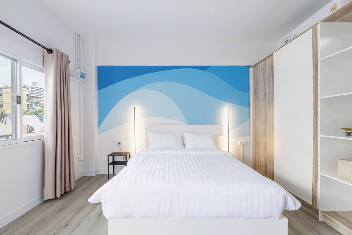Een moderne hotelkamer met een groot bed, uitzicht op de stad en een blauwe muurschildering.