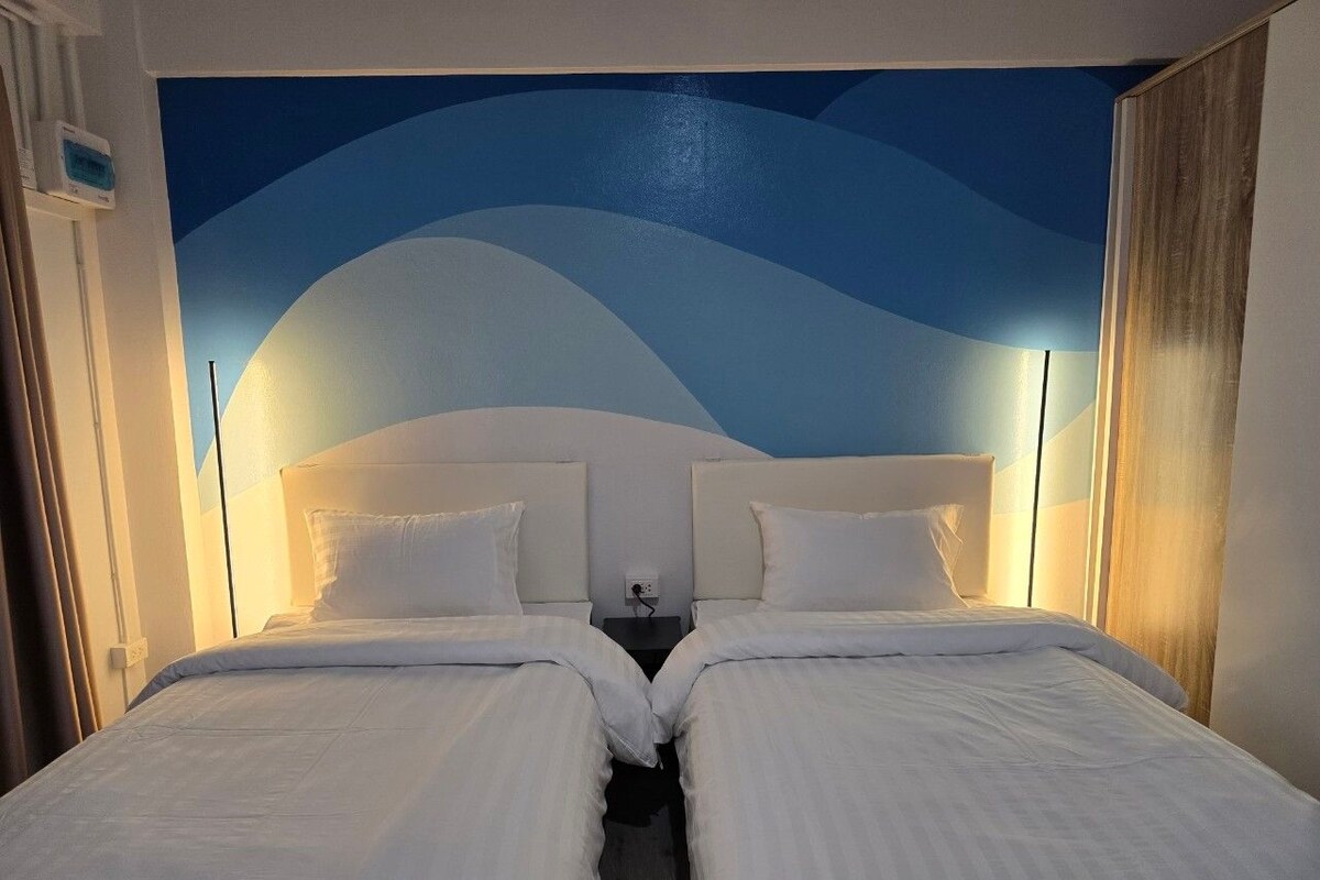 Una cama doble con sábanas blancas, cabecera con diseño de olas azules y lámparas de noche.