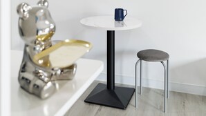 Une petite table ronde avec un pied noir, une tasse bleue et une chaise en métal.