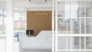 Un espace d’accueil moderne, doté d’un comptoir de réception blanc, d’un mur revêtu de panneaux en bois et de grandes fenêtres offrant une vue sur le paysage urbain.