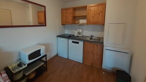 A compact kitchen with wooden cabinets, a microwave, a dishwasher, and a refrigerator. - 180m from ski lifts, floor -2, balcony, tv, ski locker, 37m², Valfréjus (Valfréjus)