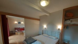 A bedroom with a bed, a nightstand, a wall-mounted shelf with towels, and a wooden floor. - 180m from ski lifts, floor -2, balcony, tv, ski locker, 37m², Valfréjus (Valfréjus)