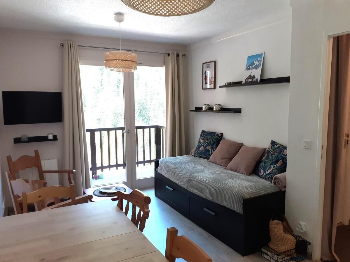 Une chambre à coucher comprenant un lit, une télévision, une table à manger, des chaises, un balcon et une fenêtre avec des rideaux.