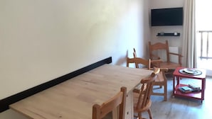 A dining area with a wooden table and chairs, a television mounted on the wall, and a window with curtains. - Ski-in/ski-out & foot of the slopes, 3rd floor, balcony, tv, ski locker, 28m², Valfréjus (Valfréjus)