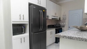 Una cocina moderna con armarios blancos, un refrigerador de acero inoxidable, un microondas y una encimera de granito.