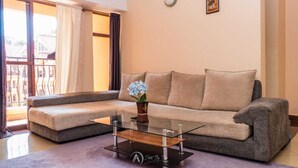 A living room with a sofa, a glass coffee table, and a vase with flowers. - Lux Suites Makao Rossyln Apartments (Nairobi)
