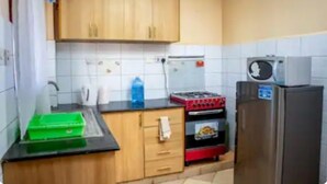 A kitchen with wooden cabinets, a black countertop, a red stove, a silver refrigerator, and a green container. - Lux Suites Makao Rossyln Apartments (Nairobi)