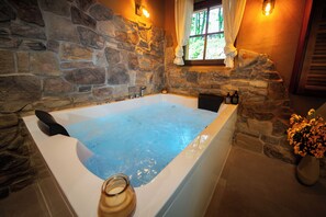 Une salle de bain aux murs en pierre, dotée d’une grande baignoire, d’une fenêtre avec des rideaux et d’un vase rempli de fleurs.