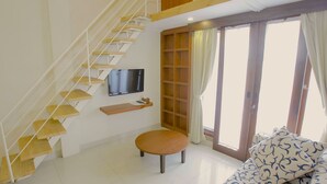 Una escalera con un televisor montado encima, un banco de madera, un sofá con cojines estampados y un ventanal corredero que da a un espacio exterior.