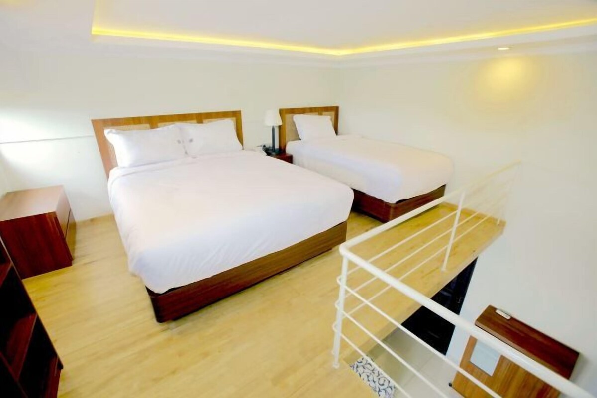 Een hotelkamer met twee bedden, houten vloeren, een wit plafond en een witte metalen plank.