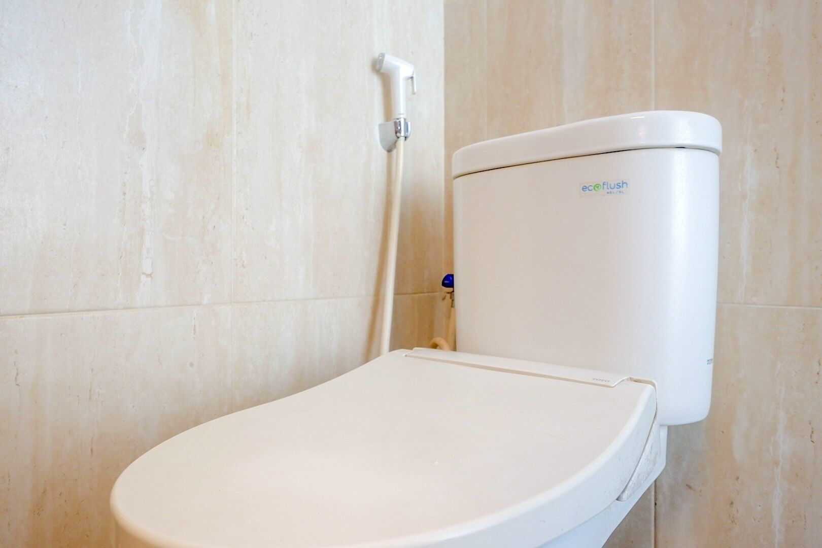 Un inodoro blanco con tanque etiquetado 'eco flush' en un baño con paredes de azulejos color beige.