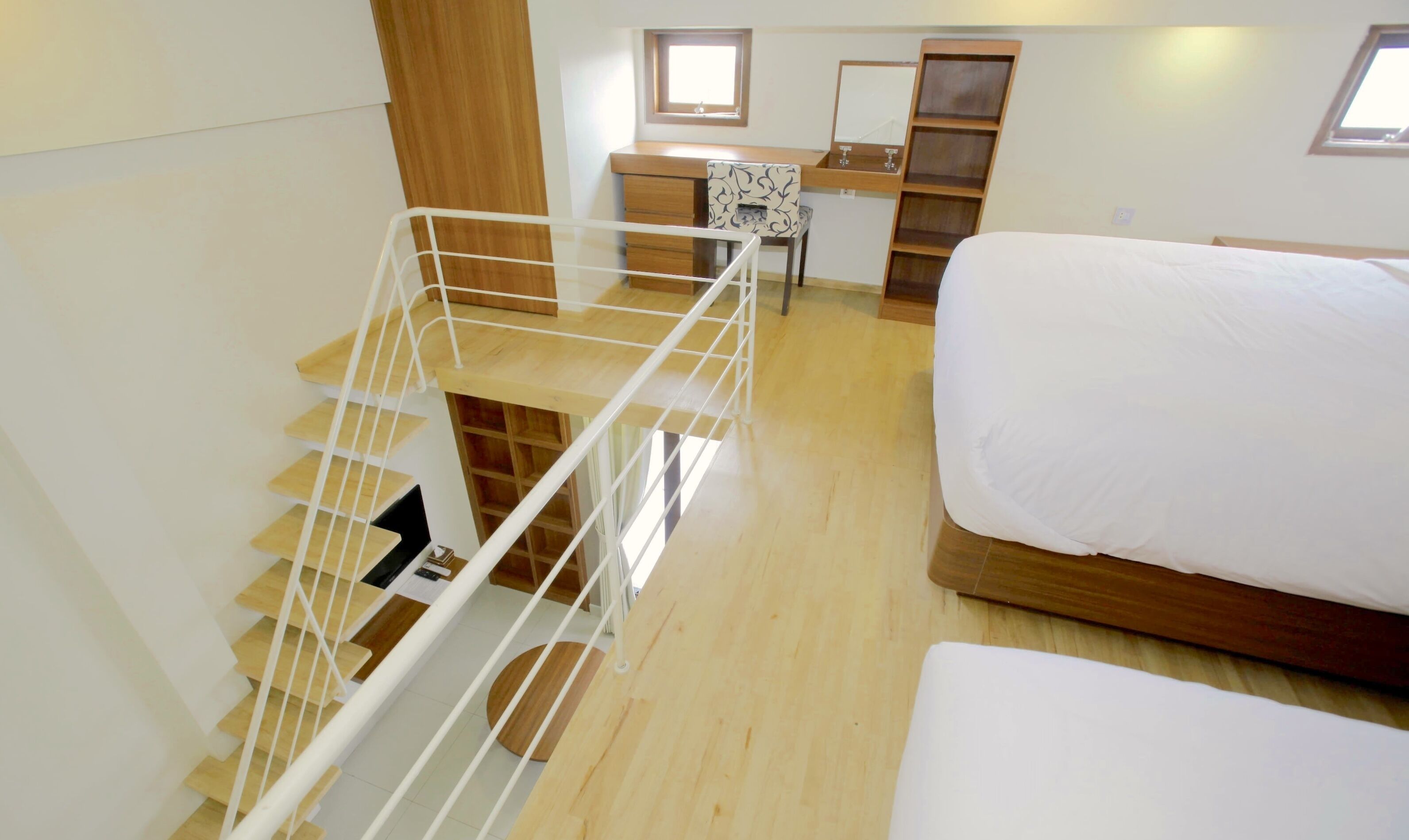 A bedroom with a wooden bed, a desk with a chair, a small table, and a staircase with a railing.