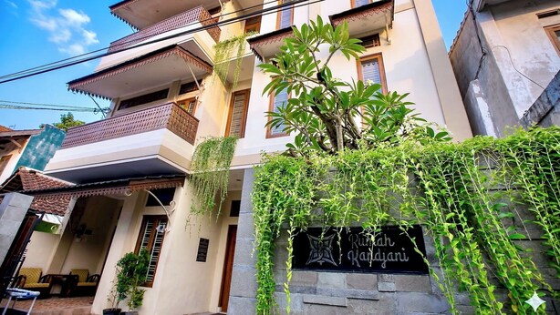 Un edificio de varios pisos con un balcón, un letrero que dice 'Ruth Kapdjani' y una planta en maceta al frente.