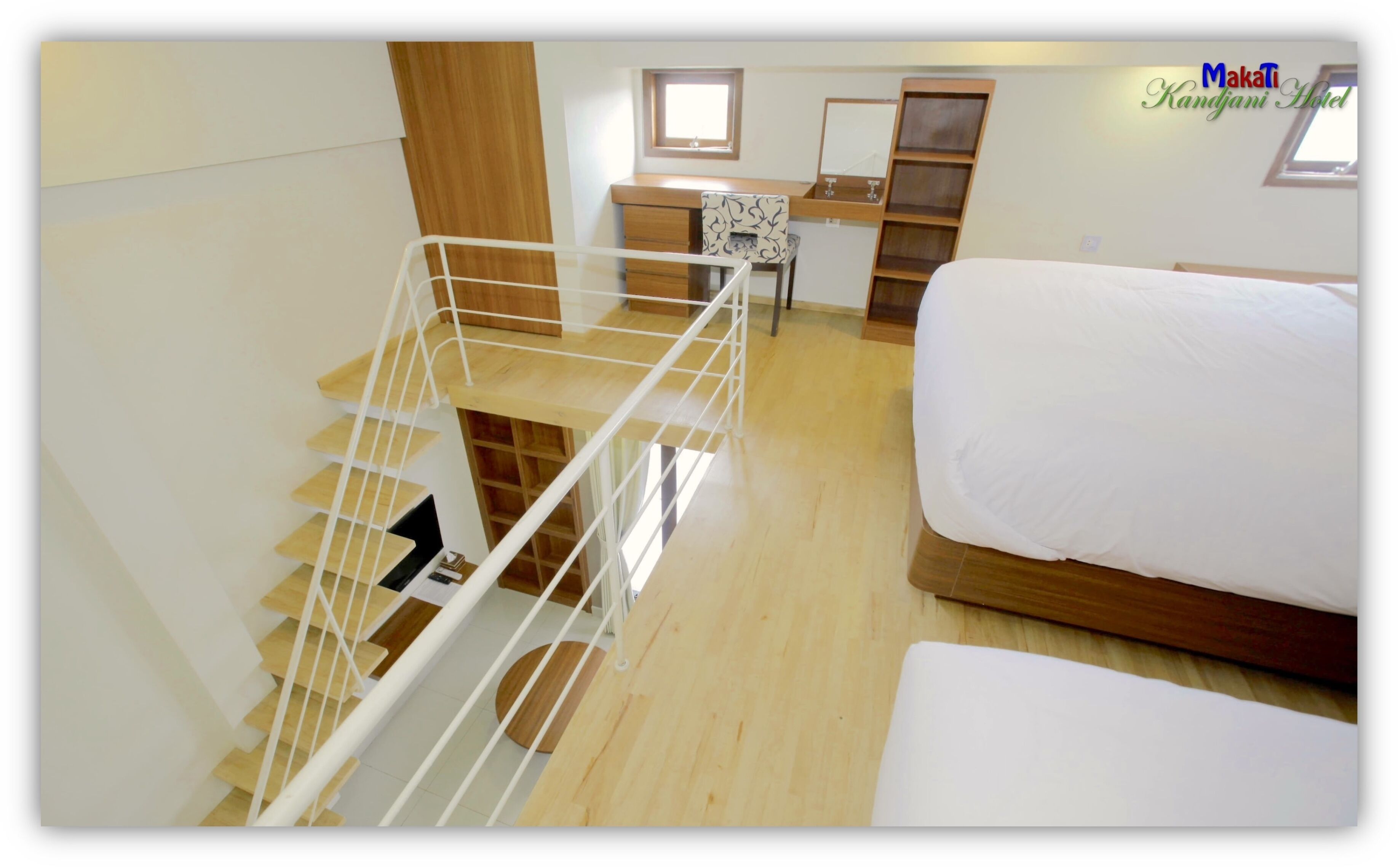 A hotel room with a wooden staircase, a bed, a desk, and a window.