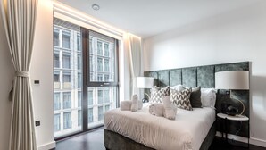 A modern hotel room with a large bed, two bedside lamps, and a view of a building through the window. - Luxury Riverfront Retreat in London (London)