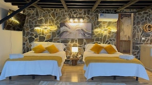 Una habitación con dos camas, una pared de piedra, un cuadro y techo de madera.