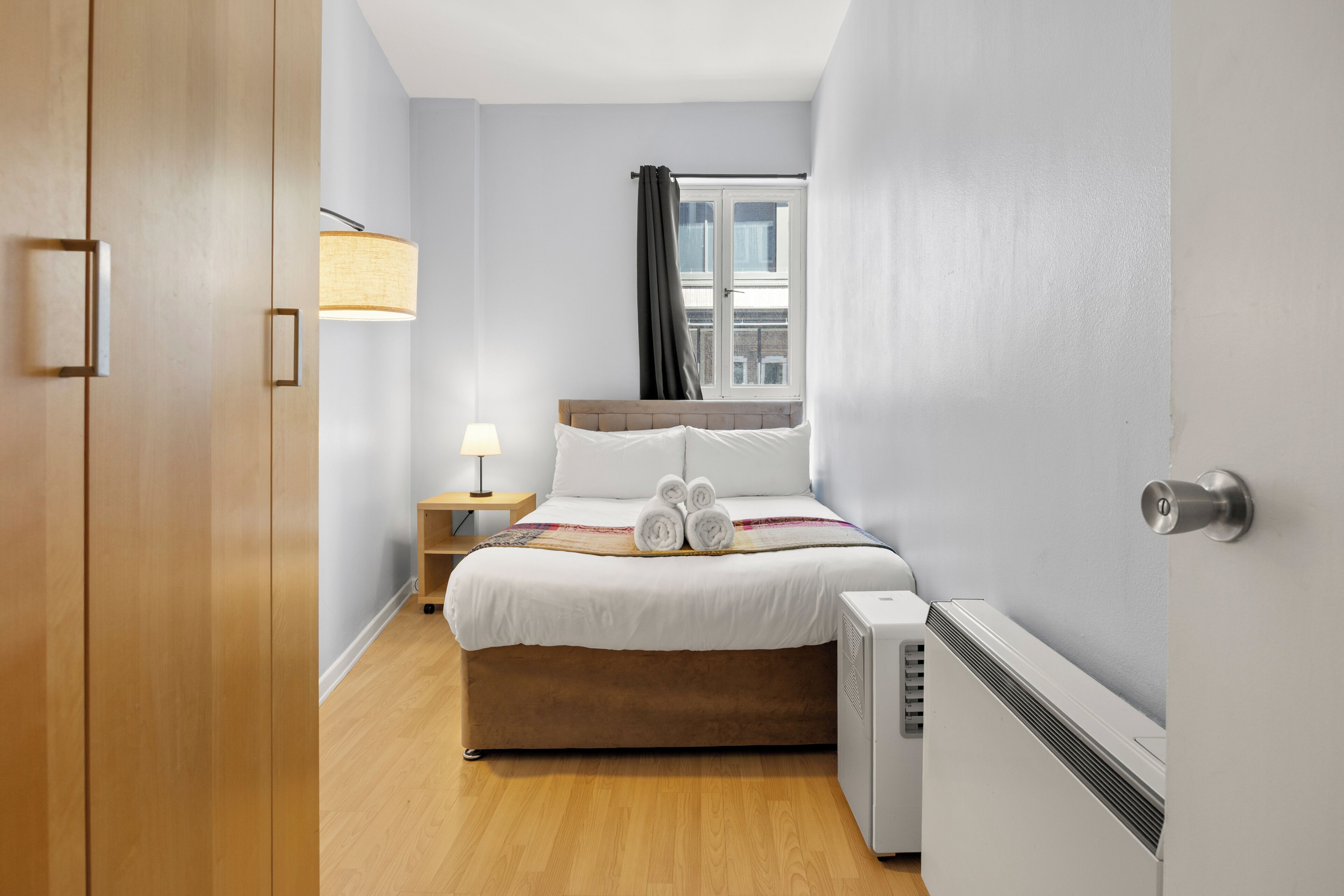 Ein Hotelzimmer mit Bett, Nachttisch, Lampe und Fenster.