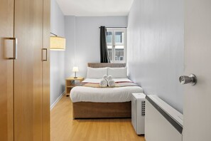A hotel room with a bed, bedside table, lamp, and window. - Prime Soho 2BR/2BA Apartment with A/C (London)