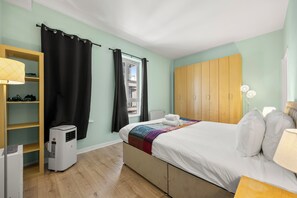 Une chambre à coucher comprenant un lit, une armoire, un bureau, une chaise, un radiateur et une fenêtre avec des rideaux.