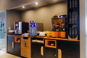Ein Selbstbedienungsbereich für Getränke mit Kaffeeautomaten, einem Obstspender und einem Glaslager.