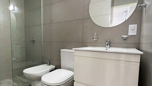 A modern bathroom with a glass shower enclosure, a bidet, a toilet, and a vanity with a mirror.