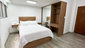 A bedroom with a wooden bed frame, a nightstand with a lamp, a wardrobe, and a mirror.