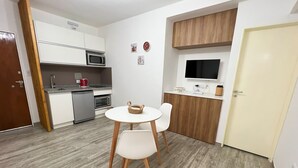 A compact kitchen with a microwave, oven, and sink. There is a small dining area with a table and chairs. A television is mounted on the wall above the counter.