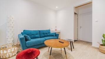 Una sala de estar moderna con un sofá azul, una mesa de centro redonda de madera, un reposapiés rojo y una cesta de mimbre.