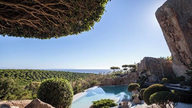 A pool surrounded by rocky terrain and greenery, with a clear view of the sea in the background. - Love Garden (Tarifa)