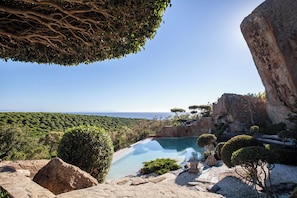 A pool surrounded by rocky terrain and greenery, with a clear view of the sea in the background. - Love Garden (Tarifa)