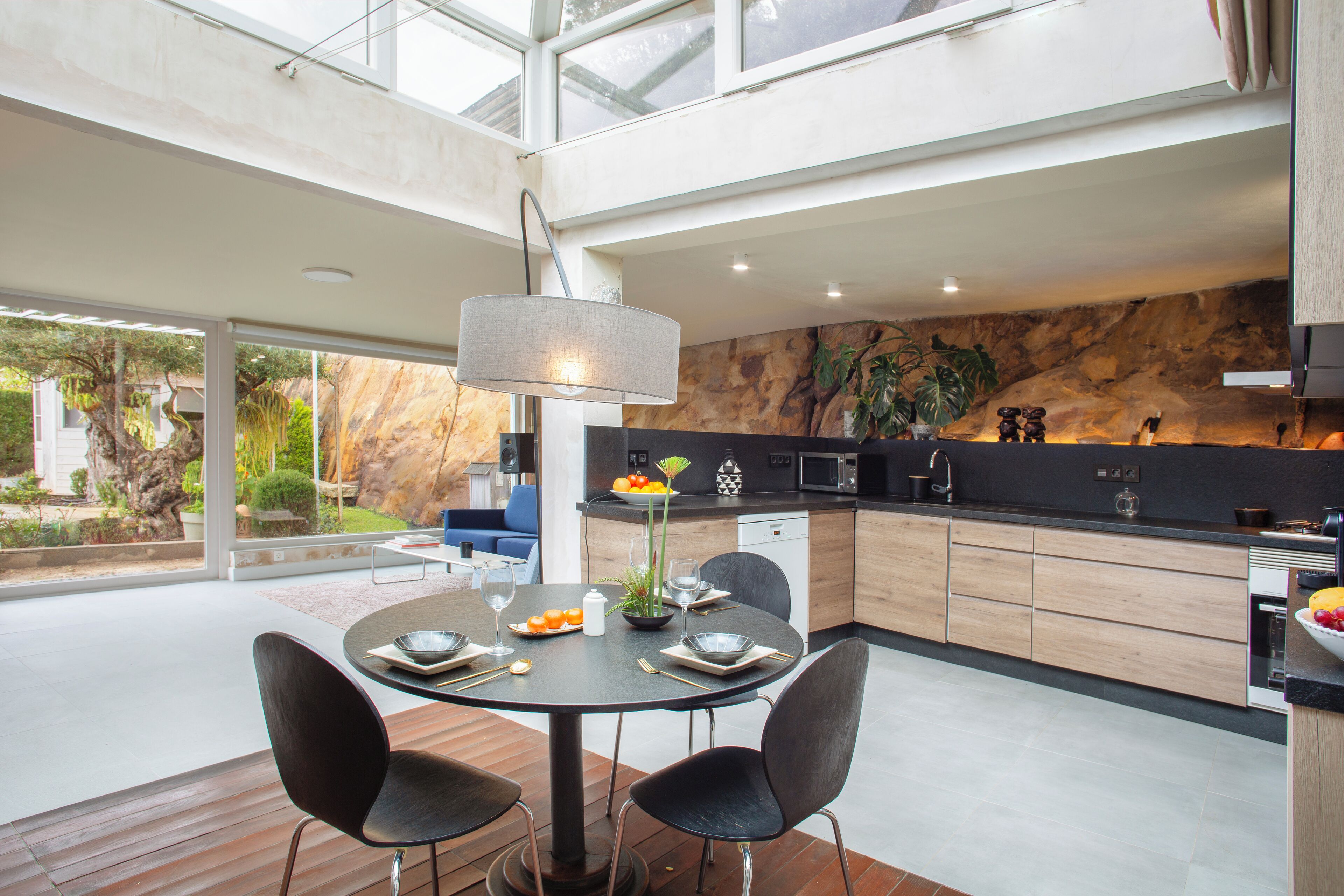 A modern kitchen with a dining area, featuring a round table, chairs, and a pendant light.