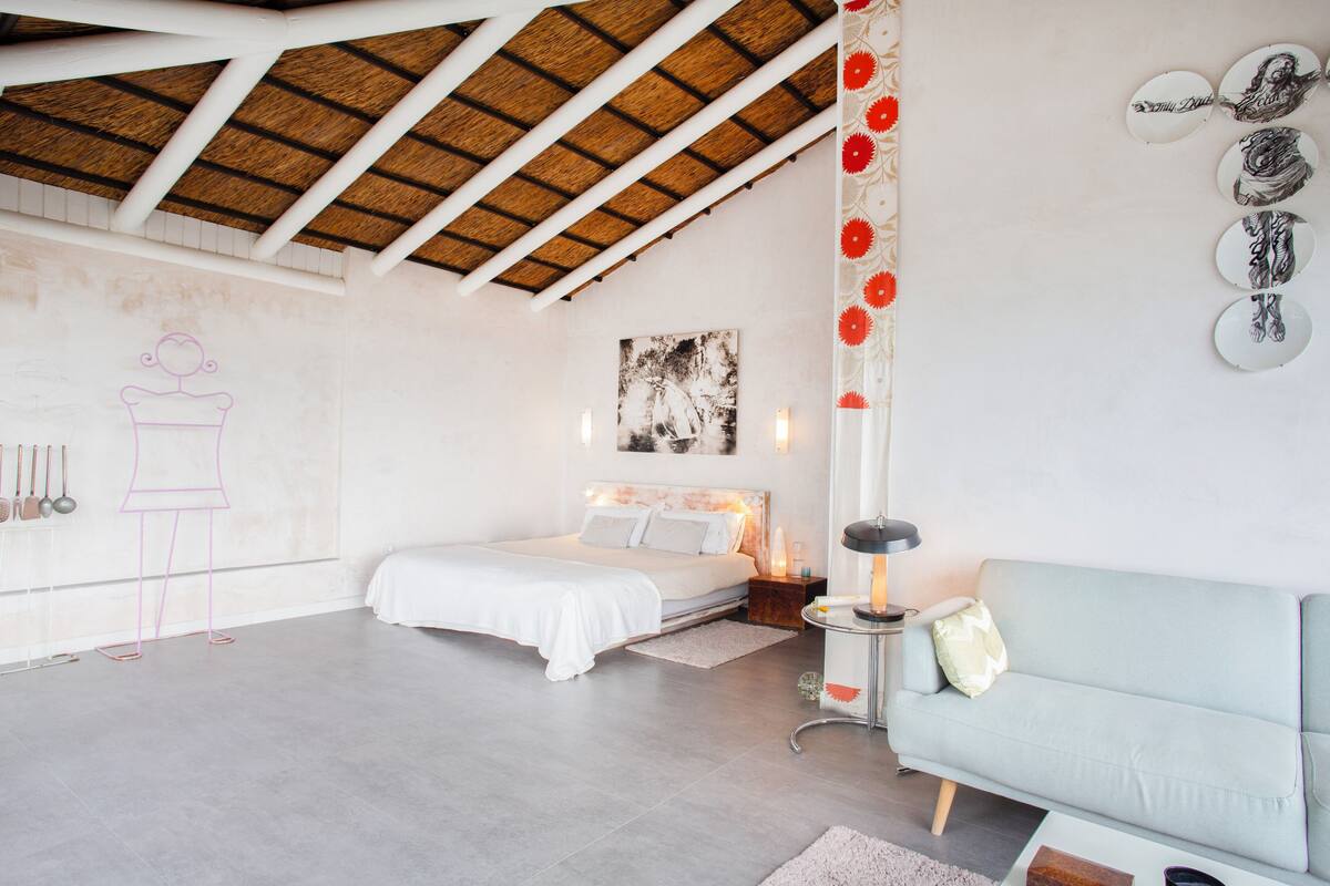 Un dormitorio con cama, mesita de noche, lámpara, sofá y pared decorada con placas.