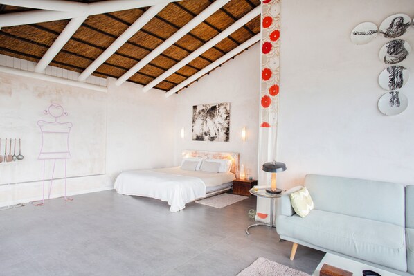A bedroom with a bed, a nightstand, a lamp, a sofa, and a wall with decorative plates. - Love Garden (Tarifa)
