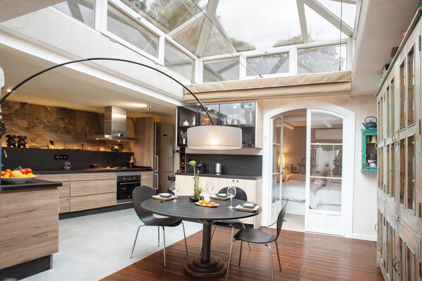 A modern kitchen with a dining area, featuring a round table, chairs, and a large window. - Love Garden (Tarifa)