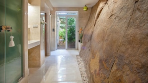A hallway with a glass door leading to a garden, a large rock wall, and a hanging light fixture. - Love Garden (Tarifa)