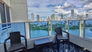 Ein Balkon mit zwei Stühlen und einem kleinen Tisch, mit Blick auf eine Stadtlandschaft und ein Gewässer.