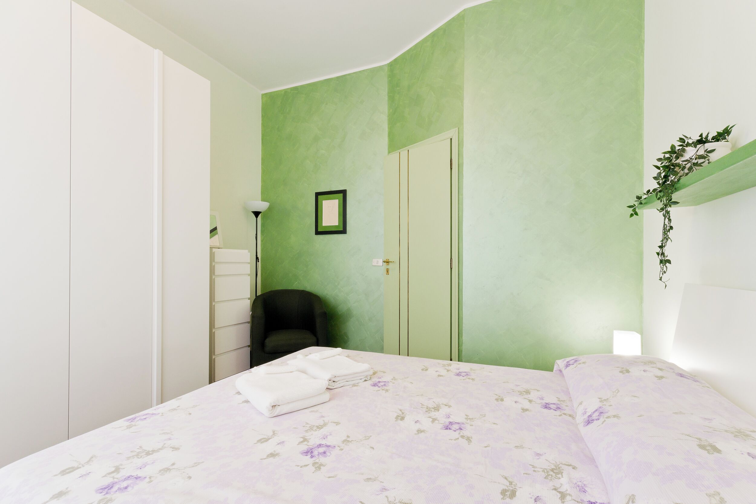 A bedroom with a bed, a chair, a wardrobe, and a green wall.