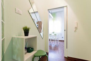 Een gang met een groene stoel, een potplant en een spiegel aan de muur.