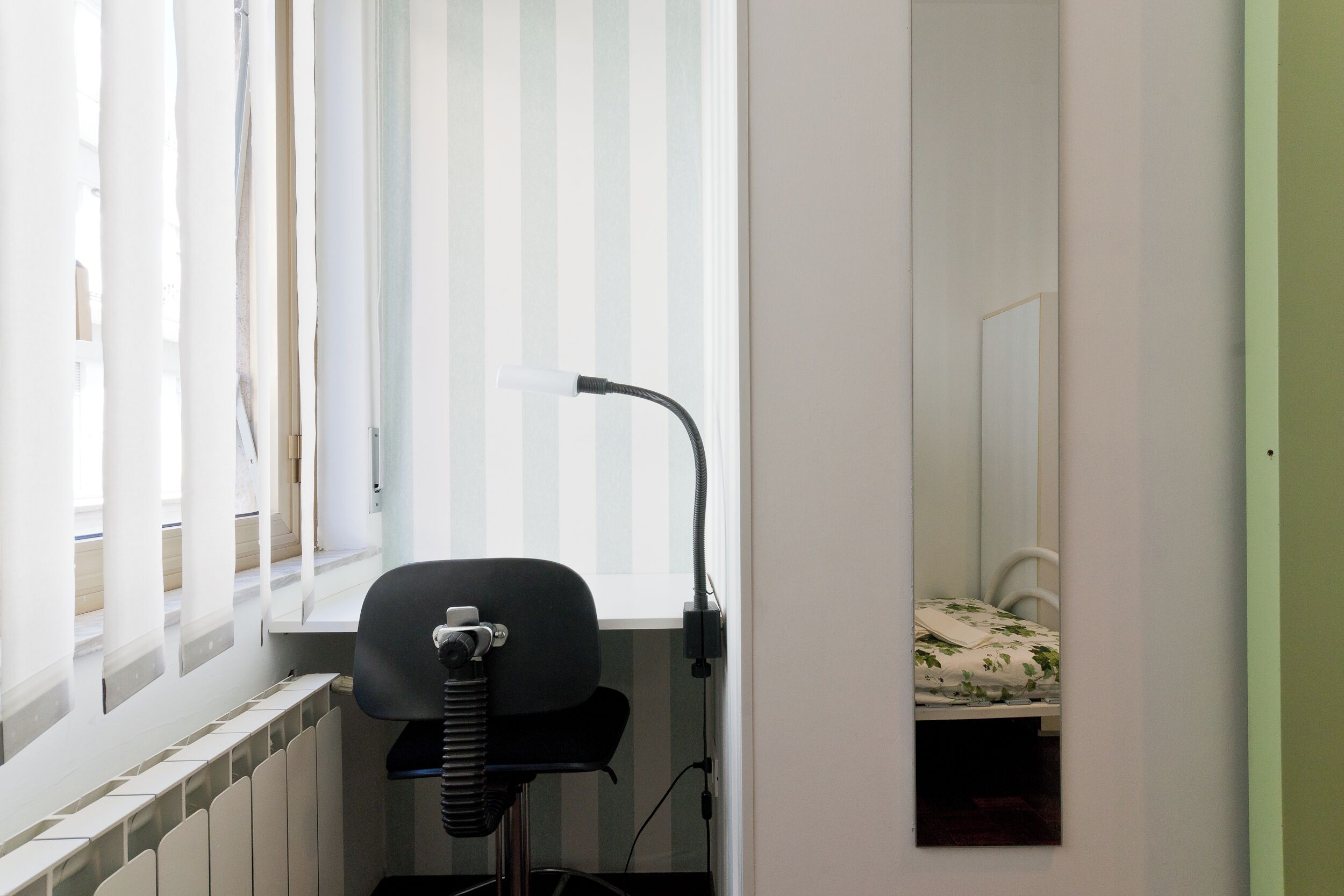 Et lille værelse med en radiator, en stol og en seng med blomstret sengetæppe.